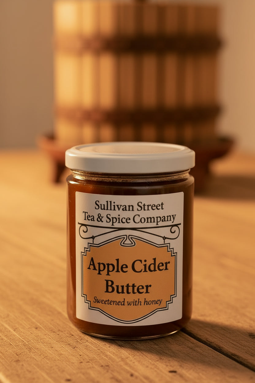 A jar of Sullivan Street Tea &amp; Spice Company Apple Cider Butter, sweetened with honey, on a white surface with a blurred indoor background.
