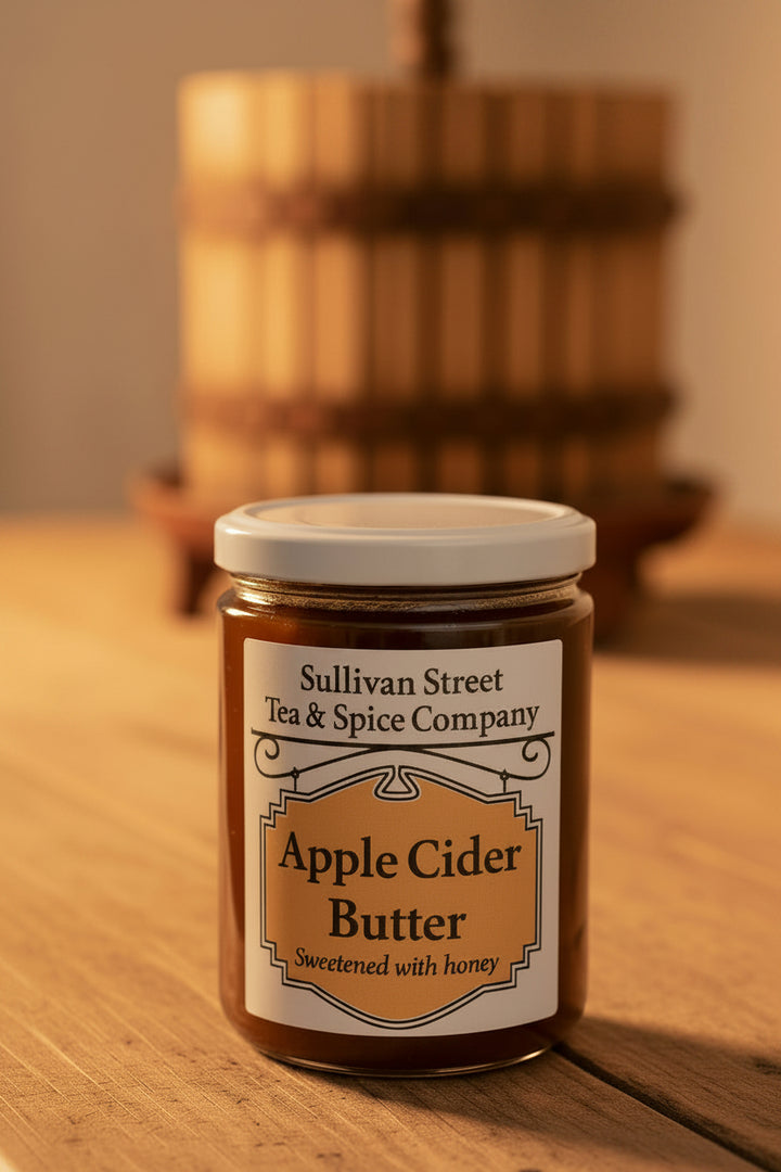 A jar of Sullivan Street Tea &amp; Spice Company Apple Cider Butter, sweetened with honey, on a white surface with a blurred indoor background.