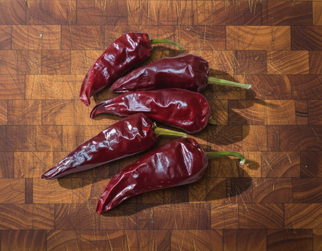 Five dried red chili peppers on a wooden surface